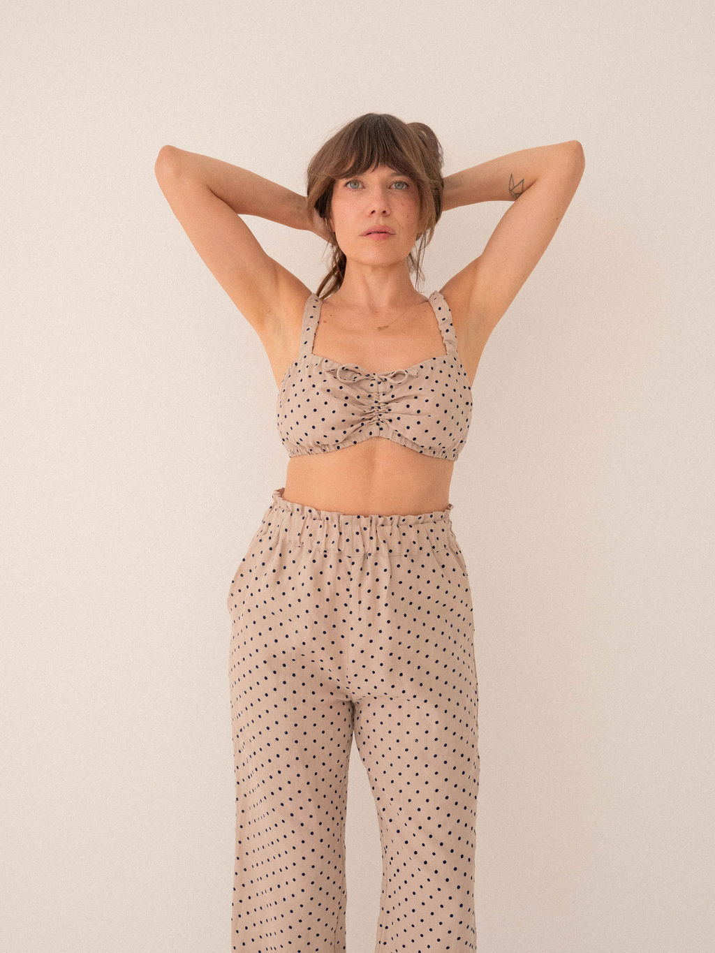 Woman wearing a polka dot top and pants against a plain background