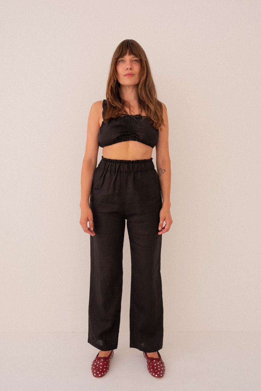 Woman wearing a black outfit with a top and wide-leg pants against a white background