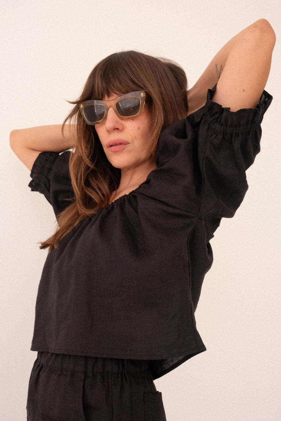 Woman wearing a black outfit with sunglasses against a white background
